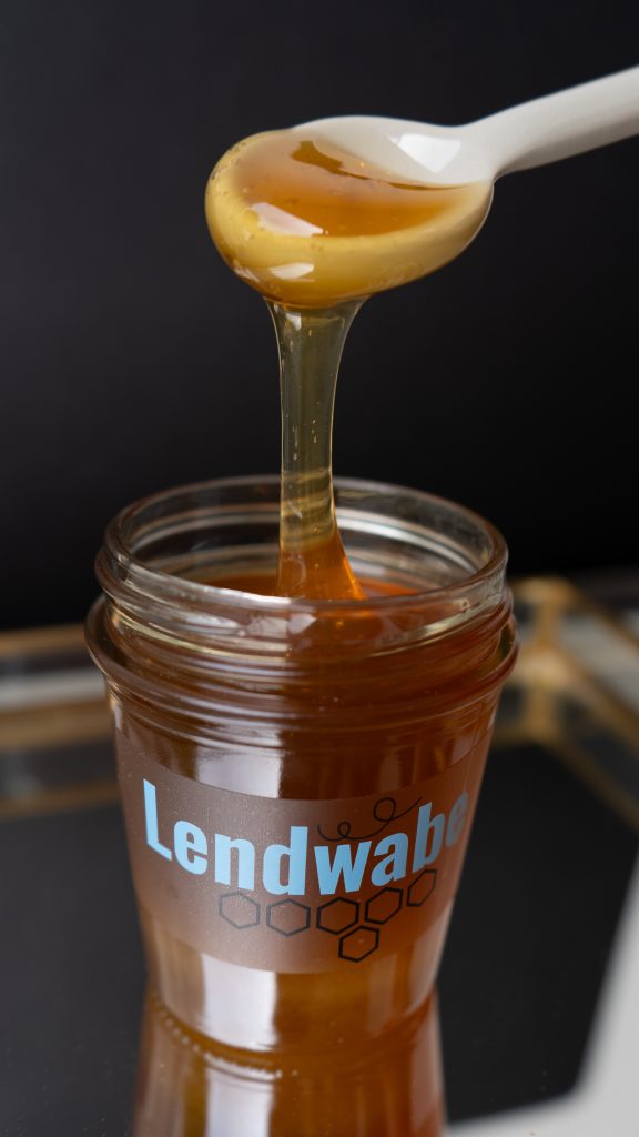 Honig tropft von einem Loeffel in ein Lendwabe-Glas